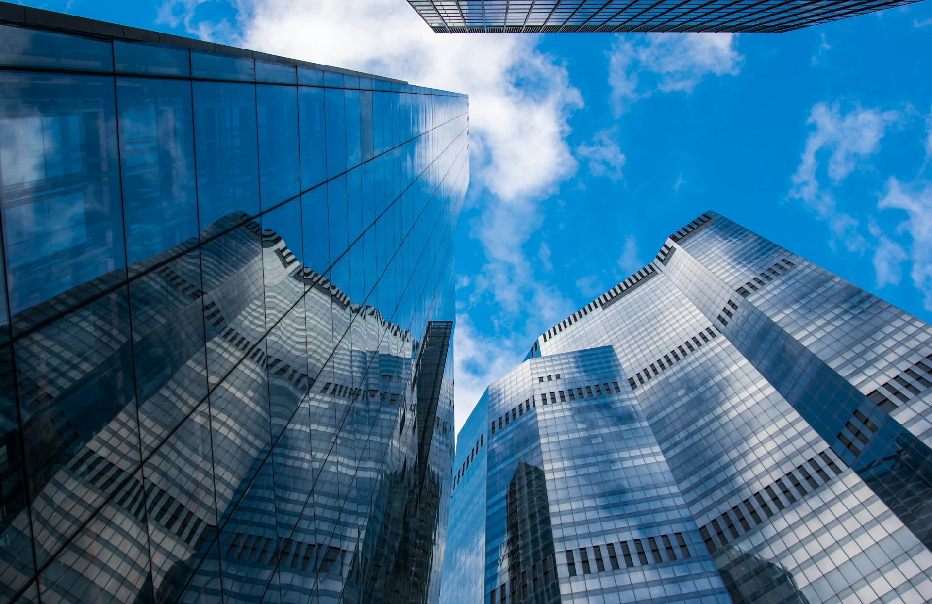 3 skyscrapers viewed from the ground, showing the blue sky above. They are glassy and reflective.